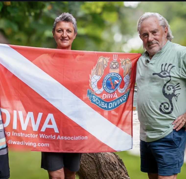 zwei Personen posieren mit einer roten Flagge der "Diving World Association".