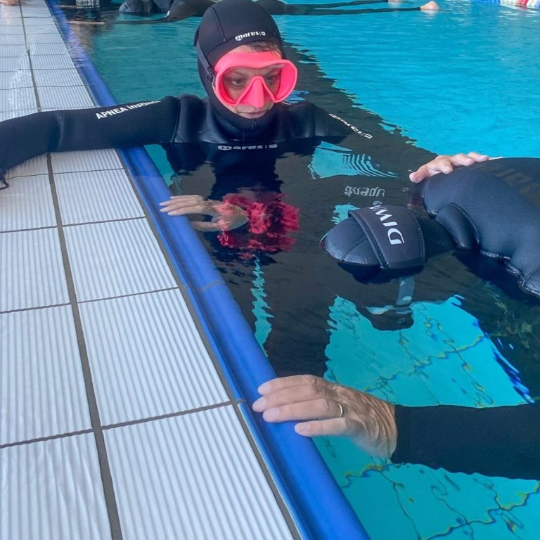 Zwei Personen im Wasser in Tauchanzügen, eine trägt eine Maske mit Schutzbrille.
