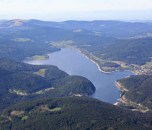 Blick auf einen Stausee umgeben von Hügeln und Wäldern.